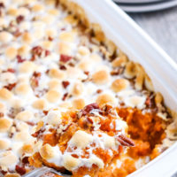 spoonful of sweet potato casserole with marshmallows scooped from white baking dish