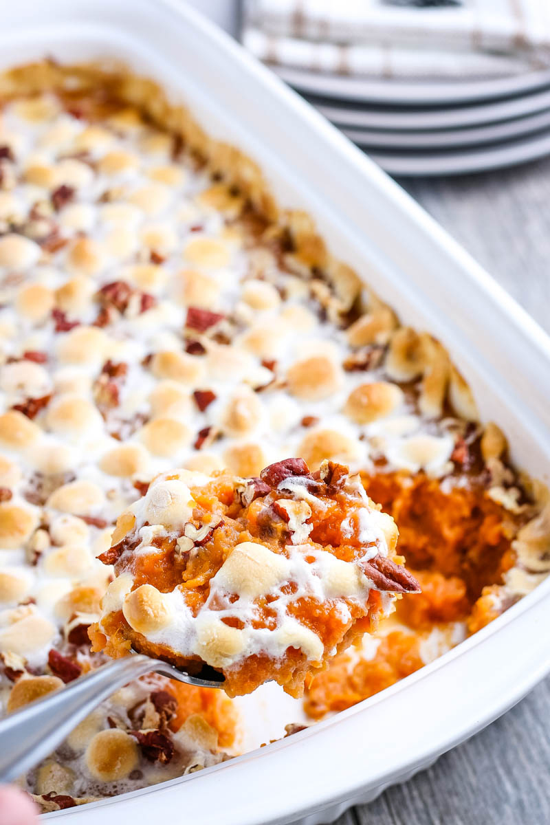 spoonful of sweet potato casserole with marshmallows scooped from white baking dish