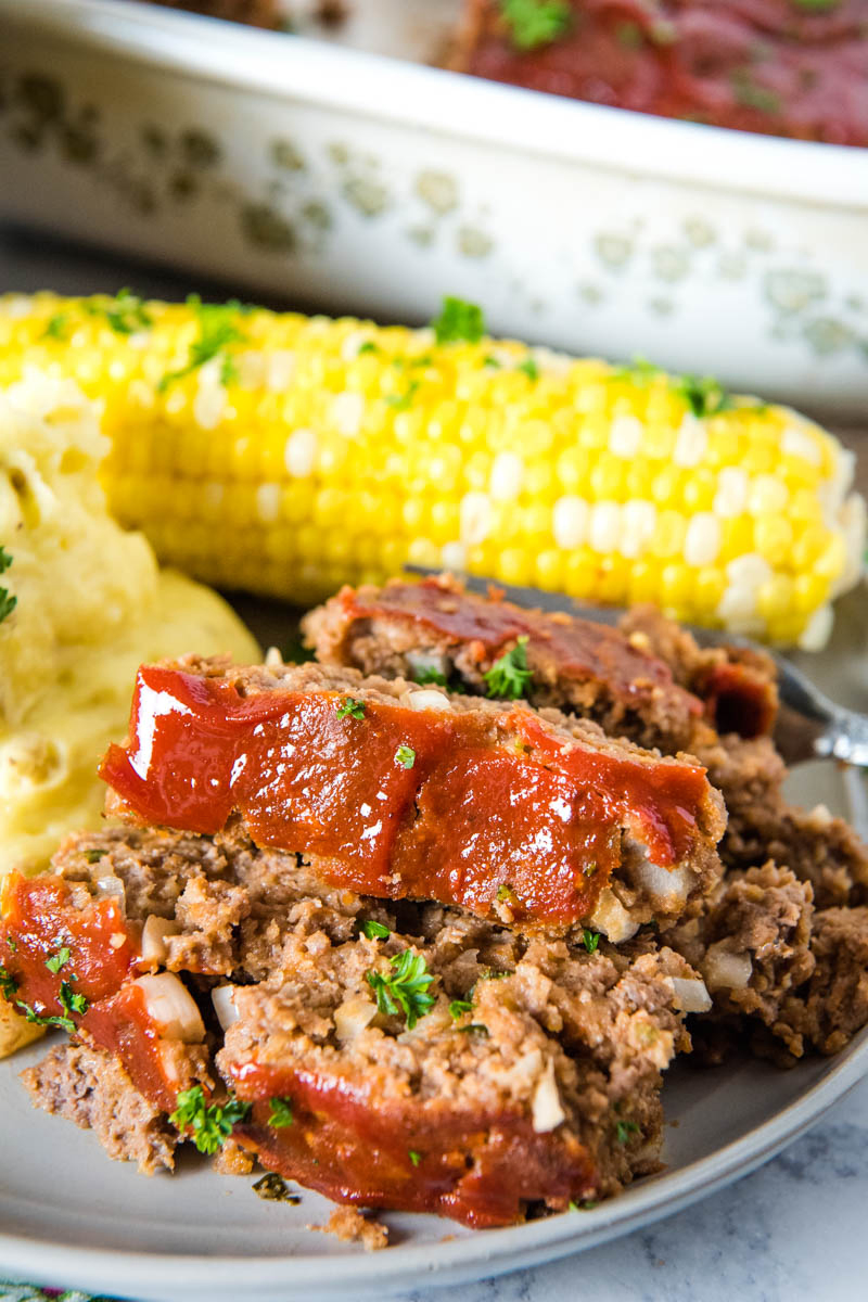 slices of traditional meatloaf on gray plate with mashed potatoes and corn on the cob