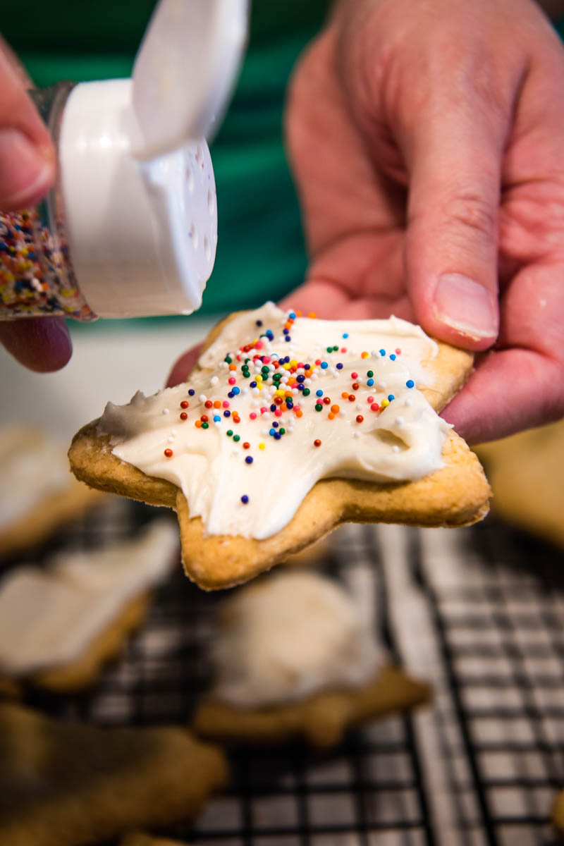 hands adding rainbow nonpareils sprinkles to frosted star shaped sugar cookie