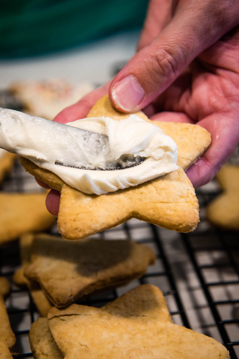 hands spreading white sugar cookie icing on star shaped Christmas sugar cookies with table knife