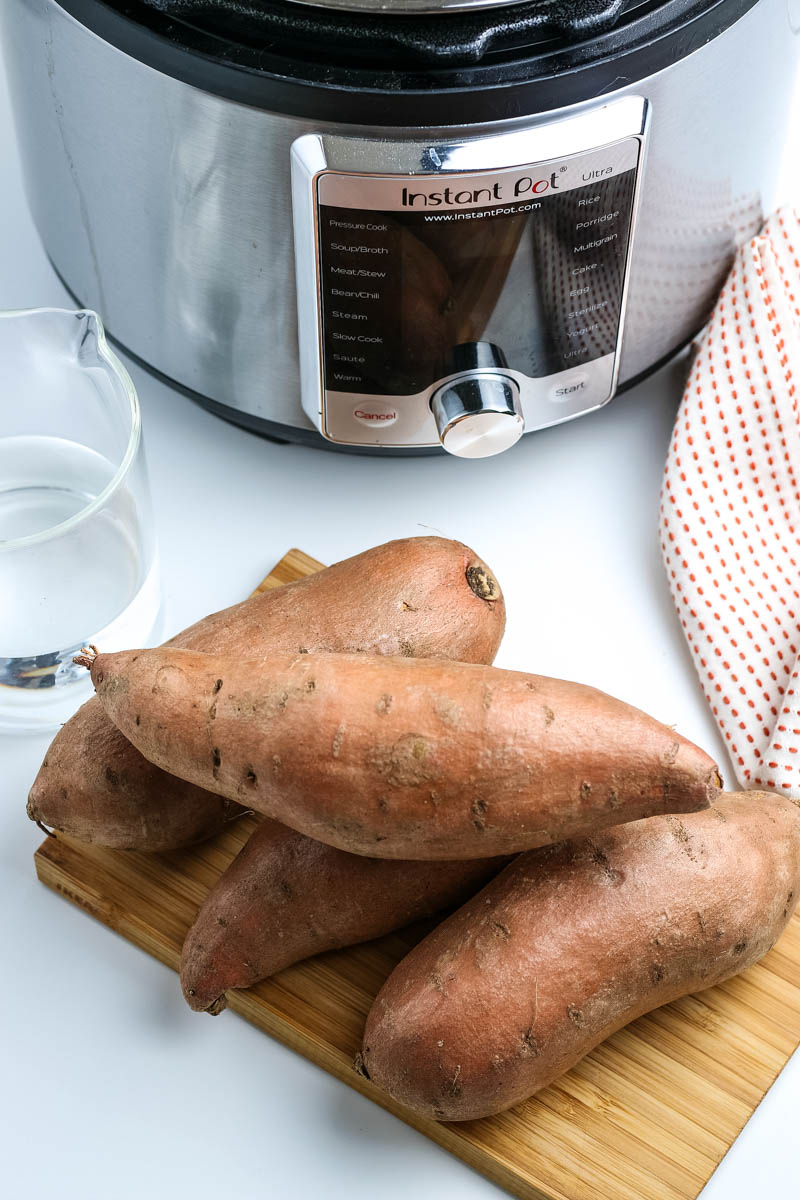 ingredients for Instant Pot sweet potatoes, including sweet potatoes on a wooden cutting board, water, and an Instant Pot