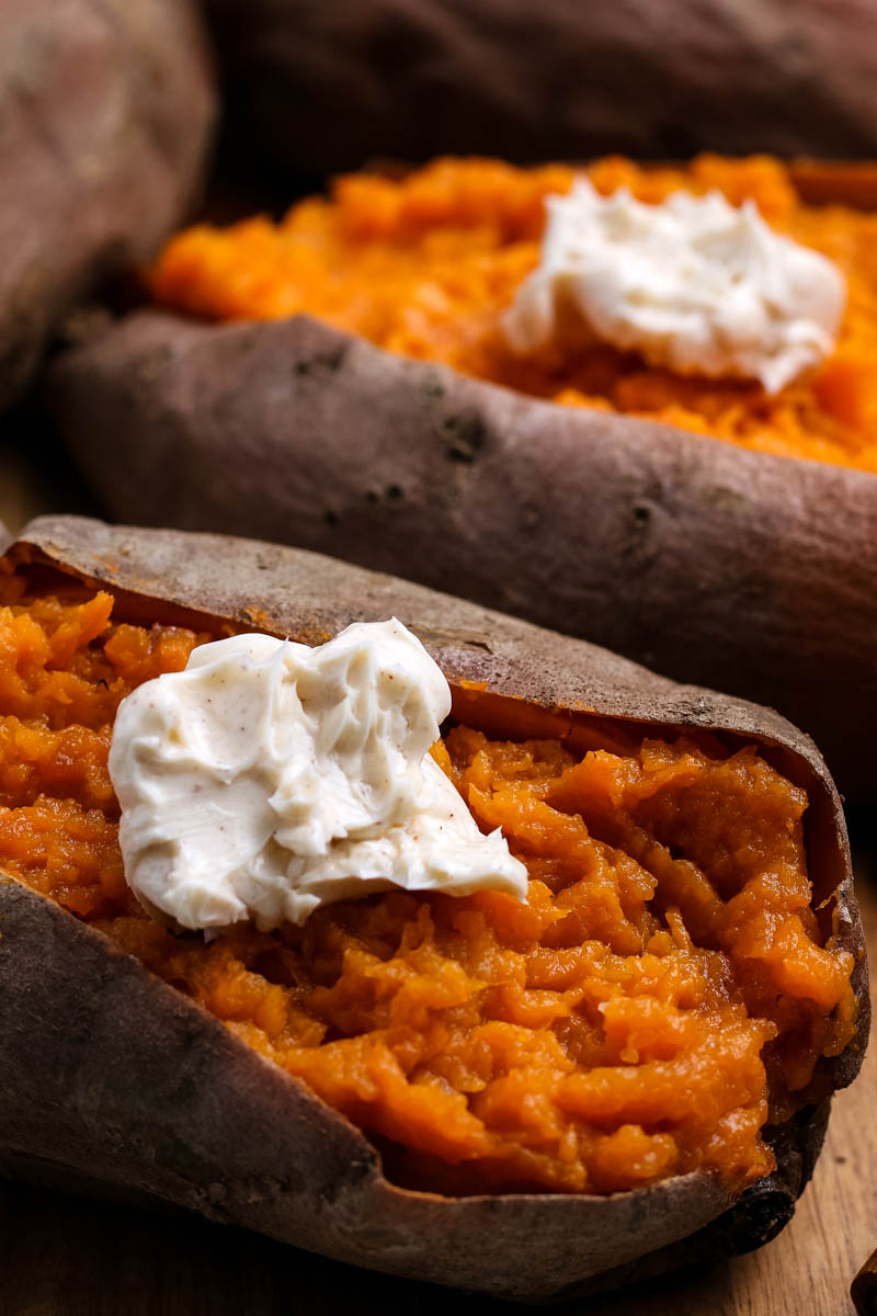 Instant Pot sweet potatoes sliced open on cutting board with dollop of whipped cinnamon butter