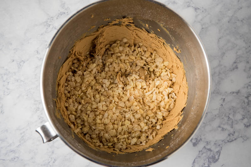 making peanut butter balls with Rice Krispies in large bowl on white marble countertop