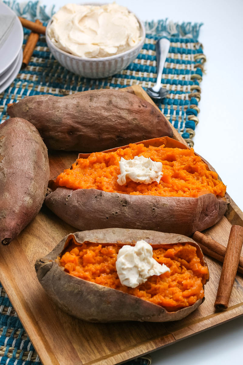 pressure cooker sweet potatoes topped with whipped cinnamon butter on wooden cutting board with cinnamon sticks and blue woven placemat