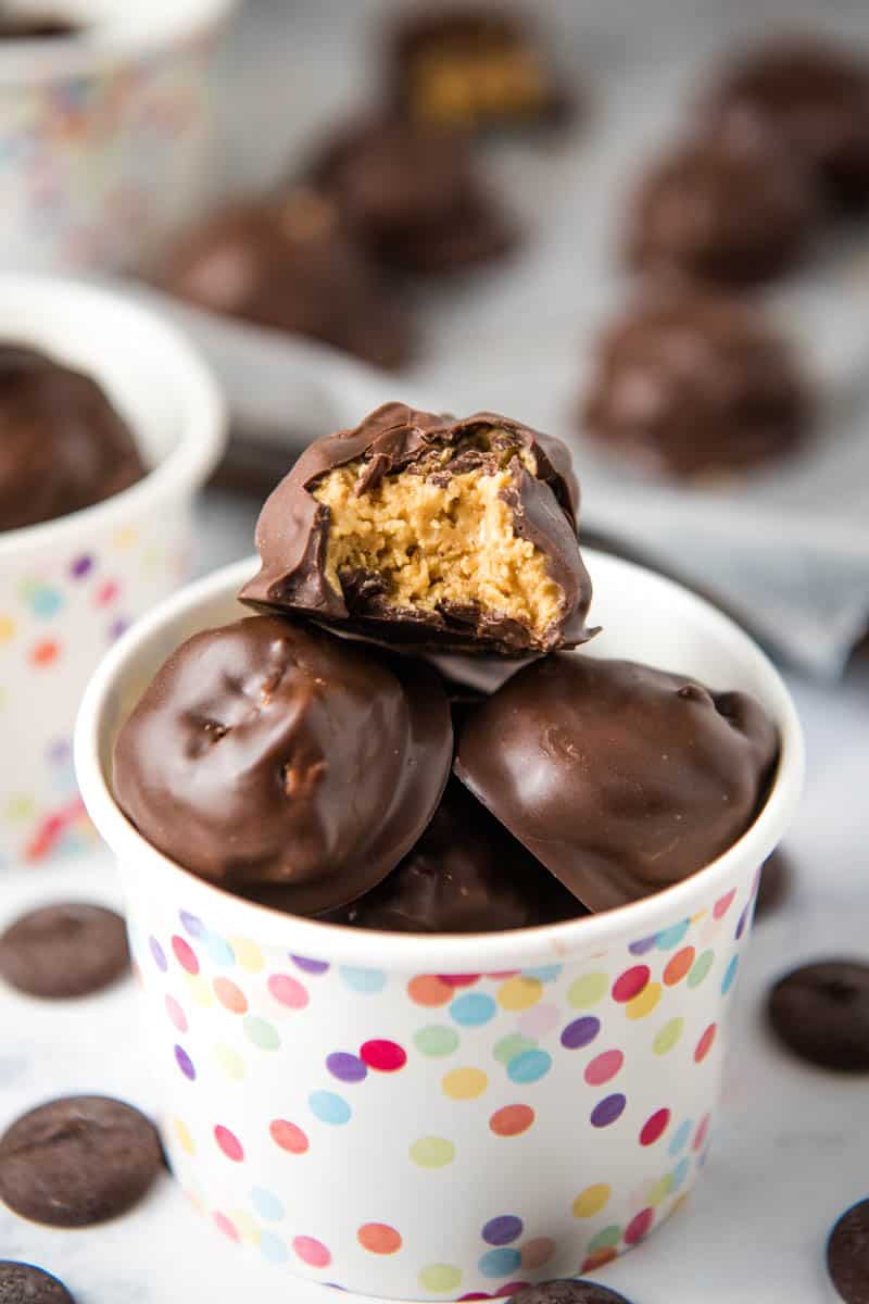 Rice Krispie peanut butter balls in rainbow polka dot snack cup with bitten candy ball on top of pile