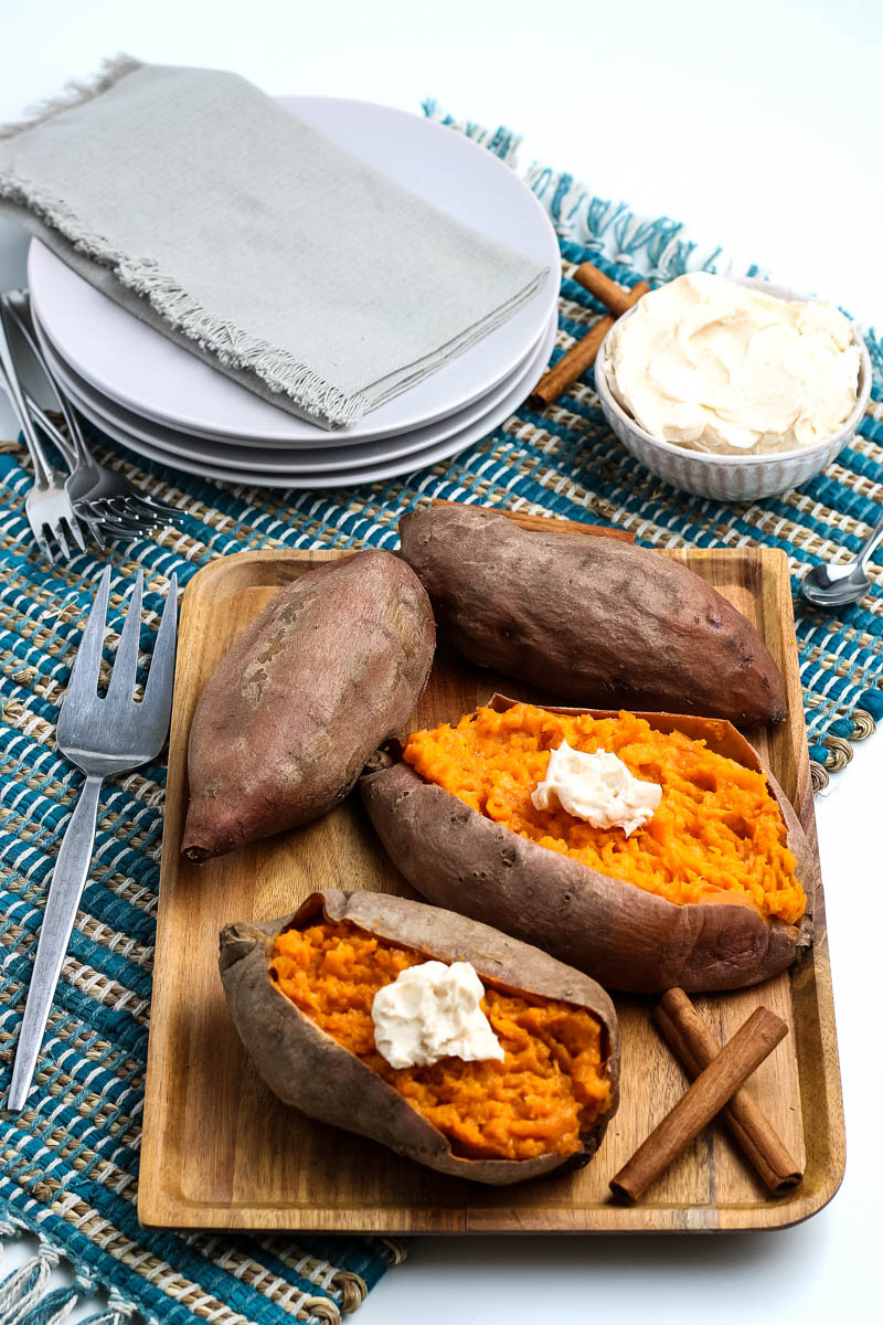 steamed sweet potatoes and whole sweet potatoes sitting on wooden tray with cinnamon sticks and woven blue placemat