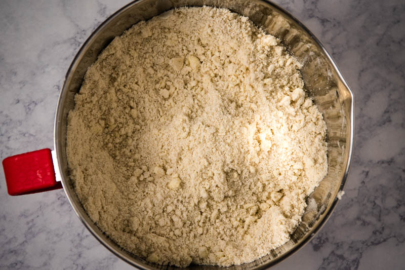 dry ingredients for sugar cookies mixed with cold butter in silver and red mixing bowl, 'til it's as fine as corn meal