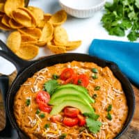 chili cheese dip in cast iron skillet, topped with fresh avocado and tomatoes