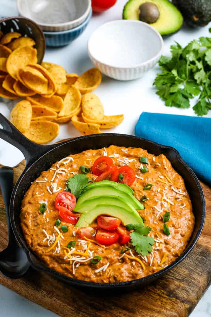 chili cheese dip in cast iron skillet, topped with fresh avocado and tomatoes