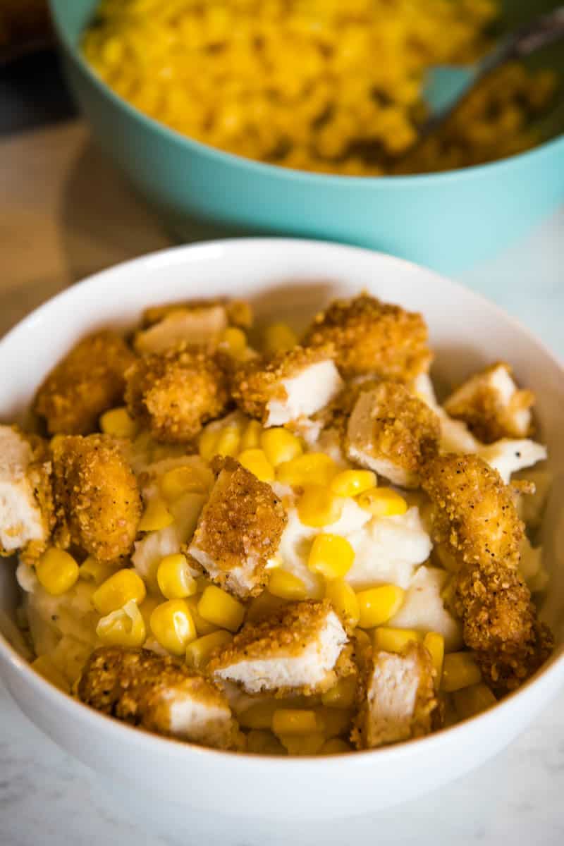 crispy bite-size chicken nuggets sprinkled on top of corn and mashed potatoes in white cereal bowl