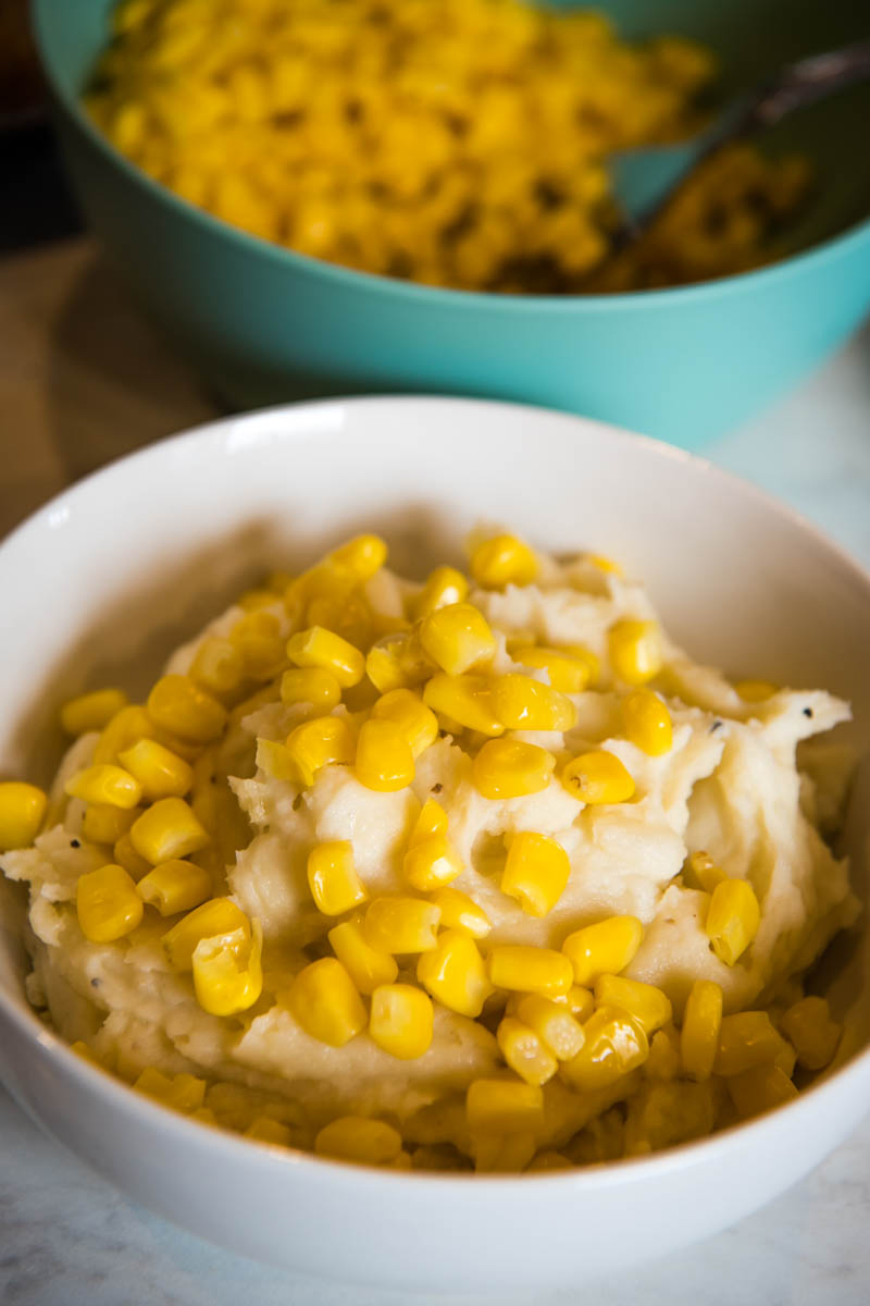 corn sprinkled on top of mashed potatoes in white serving bowl