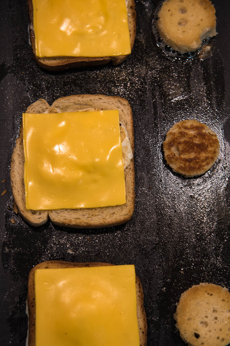 frying eggs in a basket with cheese, along with cut out bread circles, on griddle