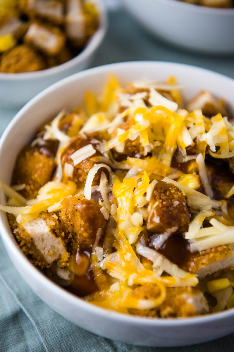 KFC Famous bowl, including mashed potatoes, corn, crispy chicken nuggets, brown gravy, and shredded cheese in white bowl