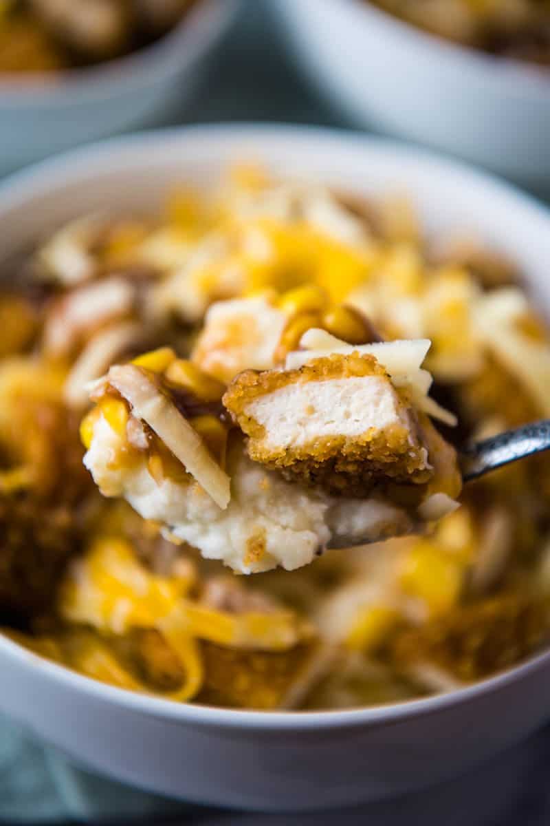 spoonful bite of chicken, mashed potatoes, corn, gravy, and cheese over KFC potato bowl in white serving bowl