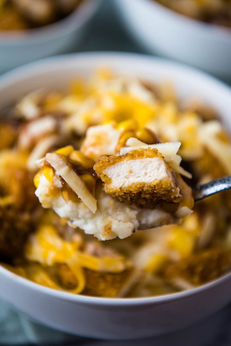 spoonful bite of chicken, mashed potatoes, corn, gravy, and cheese over KFC potato bowl in white serving bowl