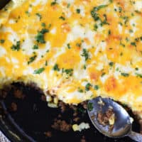 cheesy sloppy joe casserole with potatoes being spooned out of a large cast iron skillet
