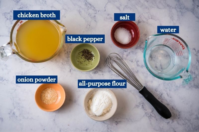 chicken gravy ingredients, including chicken broth, black pepper, salt, water, onion powder, and all-purpose flour on white marble countertop with black whisk