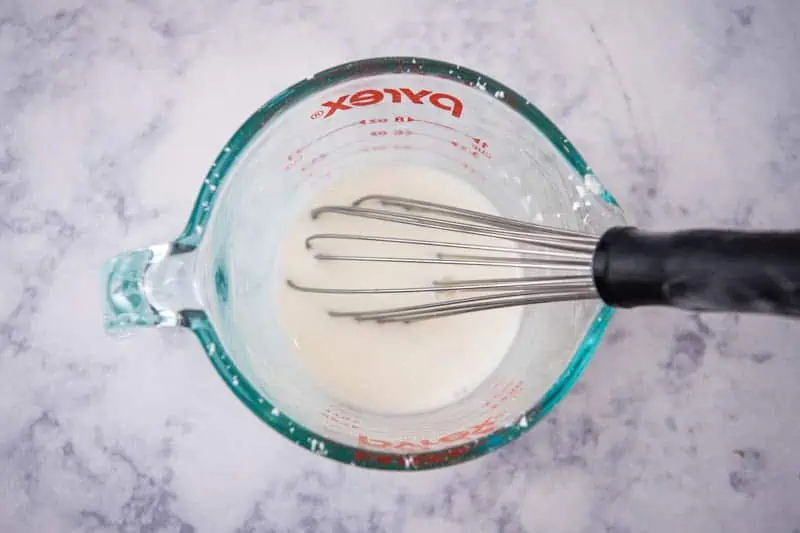 chicken gravy slurry in Pyrex glass measuring cup with black whisk