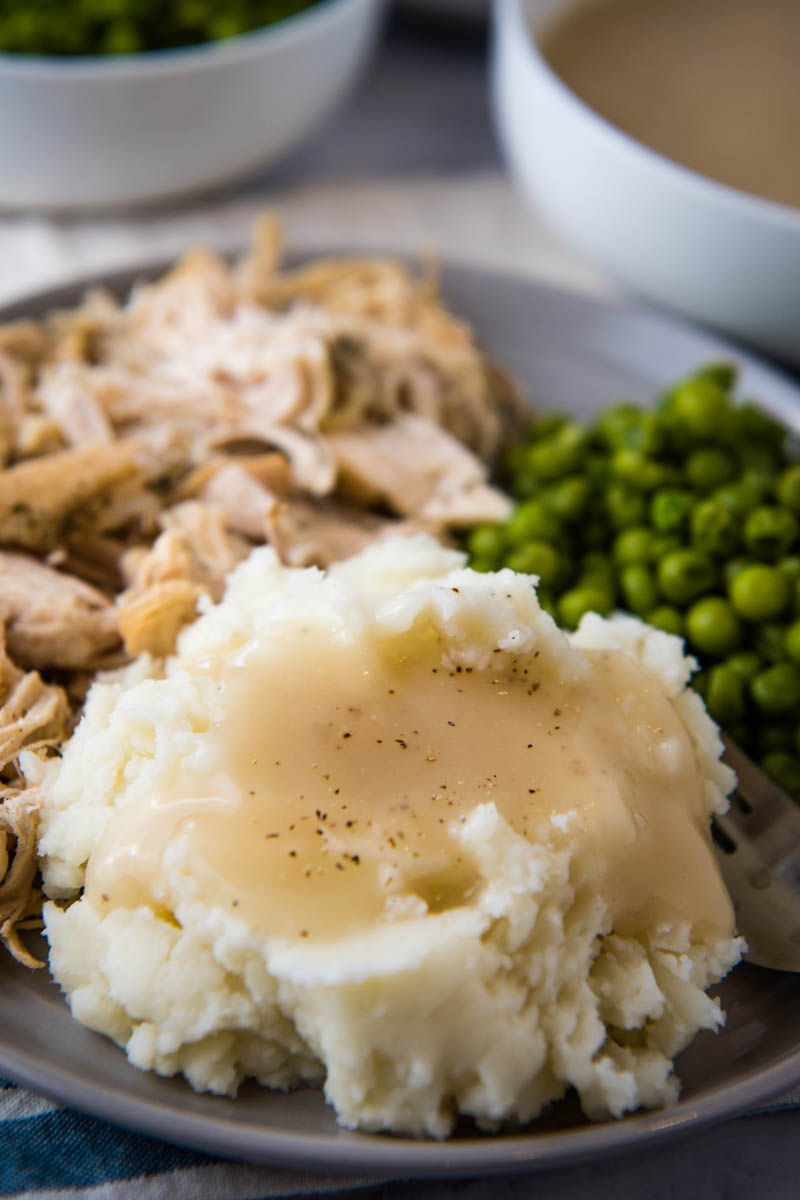 chicken gravy poured over mashed potatoes on gray plate with shredded chicken and green peas