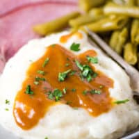 ham gravy drizzled on a pile of mashed potatoes on a rounded gray decorative plate