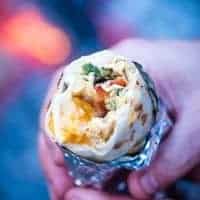 hands holding breakfast burrito wrapped in foil