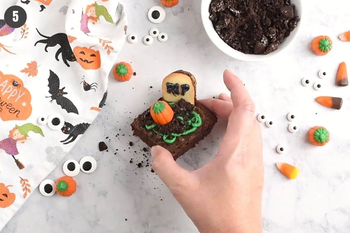 hand holding finished Halloween graveyard brownie with candy pumpkin on top