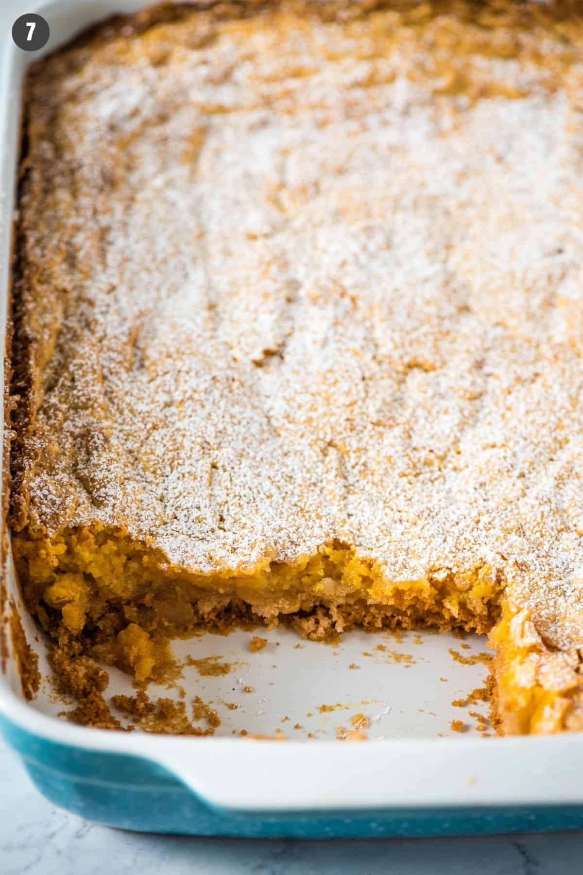sliced ooey gooey pumpkin cake, topped with powdered sugar, in blue and white baking dish