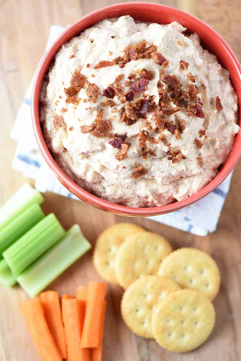 bowl of bacon cheddar bbq ranch dip with crackers and raw veggies on wooden cutting board