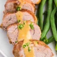 slices of brown sugar dijon pork tenderloin with gravy on white plate with green beans