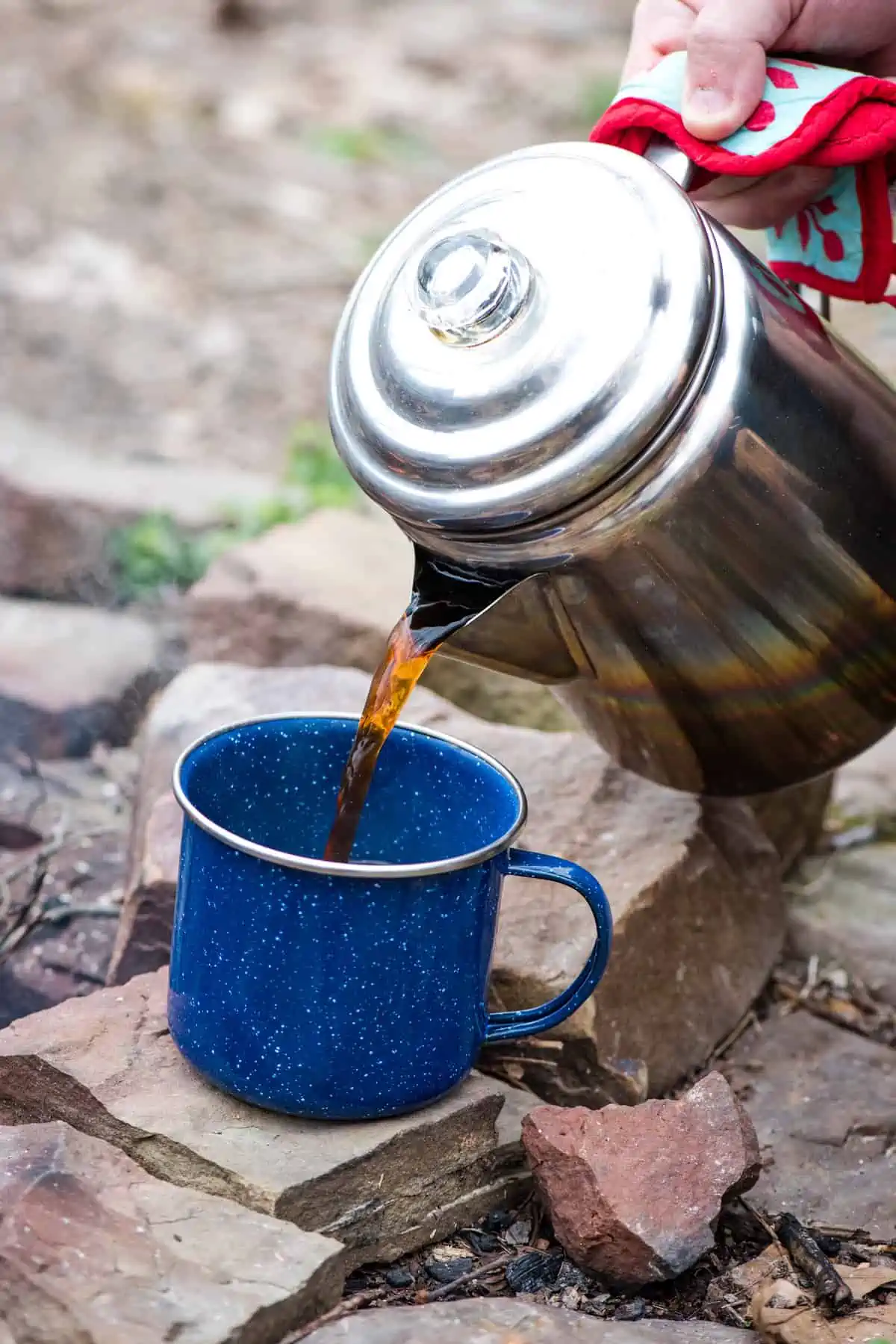 pouring camp coffee from a percolator into a blue enamelware mug