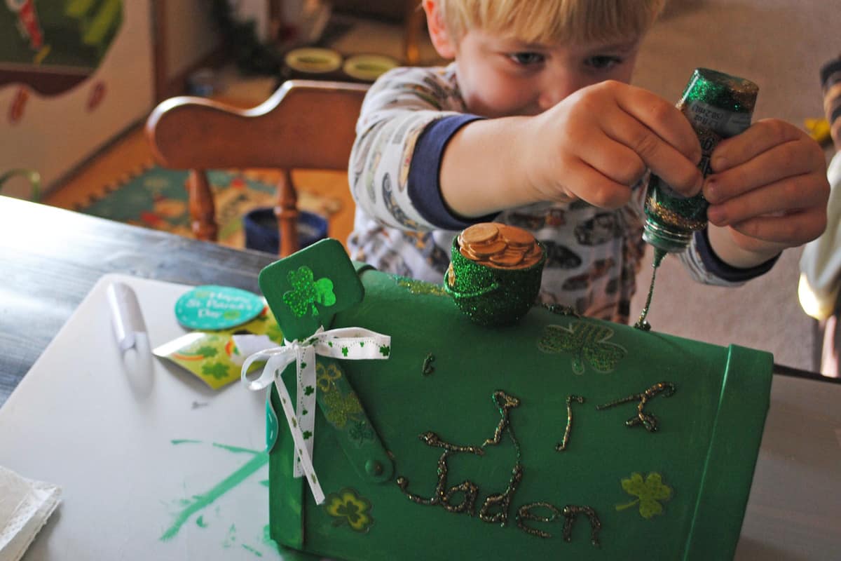 child decorating leprechaun box with green glitter glue for St. Patrick's Day craft