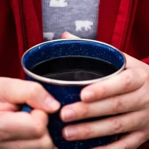 holding blue enamelware mug full of campfire coffee in hands