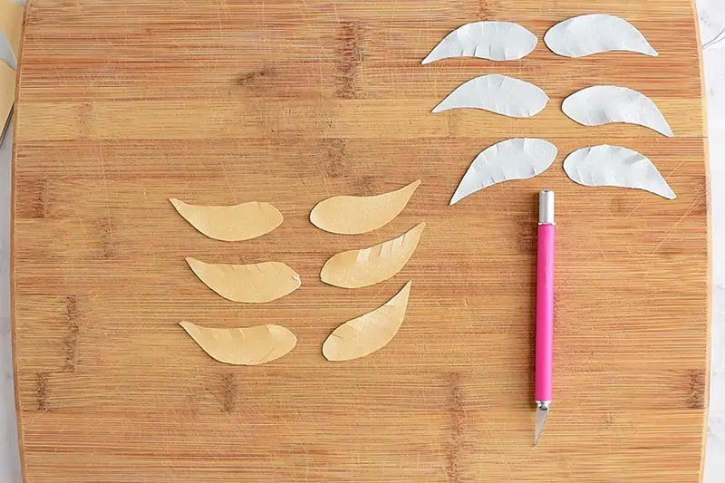 cut Golden Snitch wings out of template with pink craft knife on wooden cutting board