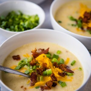 white bowl of Instant Pot potato soup with bacon, shredded cheese, and green onions