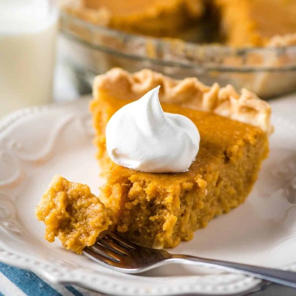 slice of sweet potato pie with whipped cream on white plate with fork