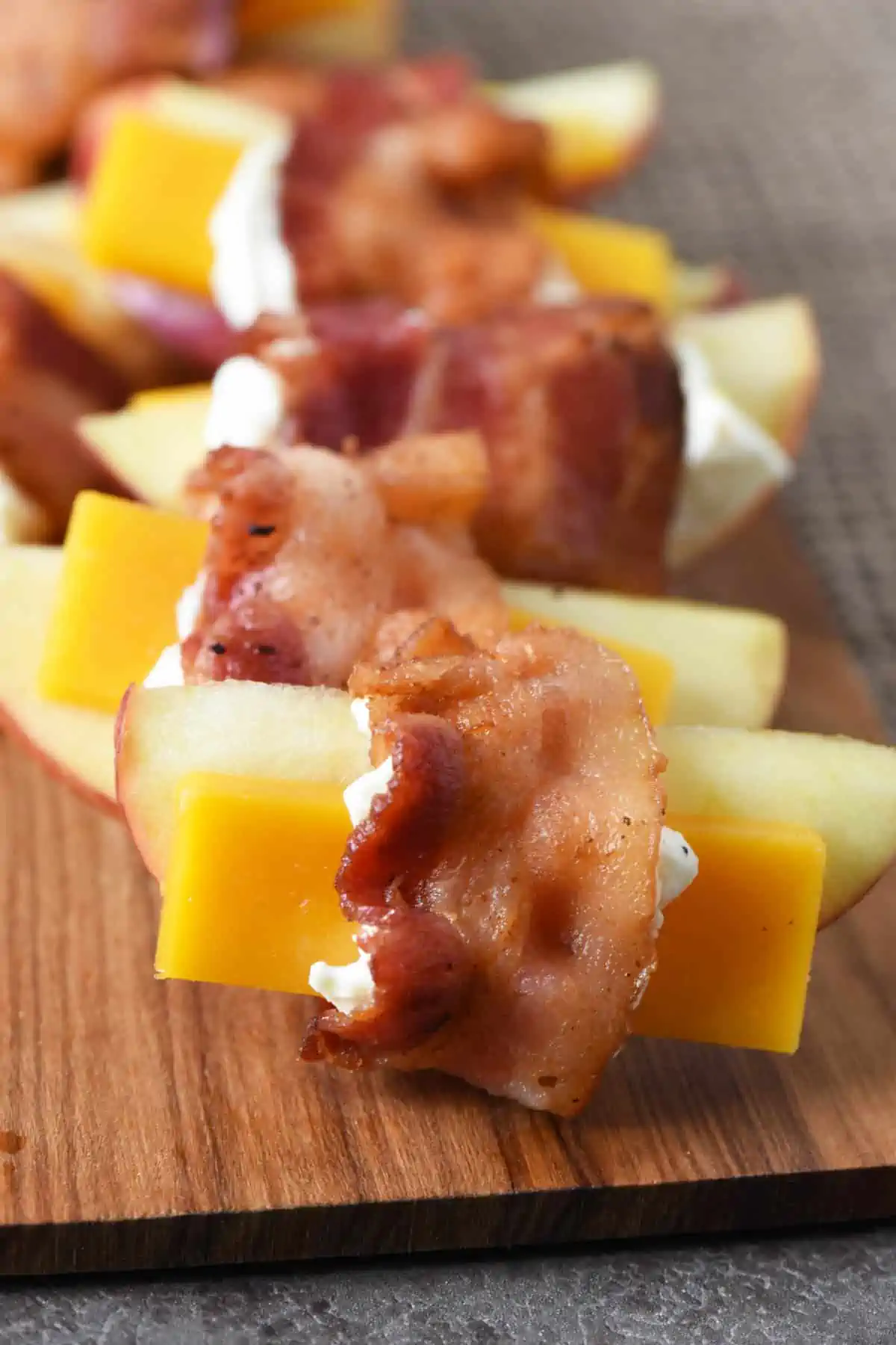 bacon wrapped apples with cheese on wooden cutting board