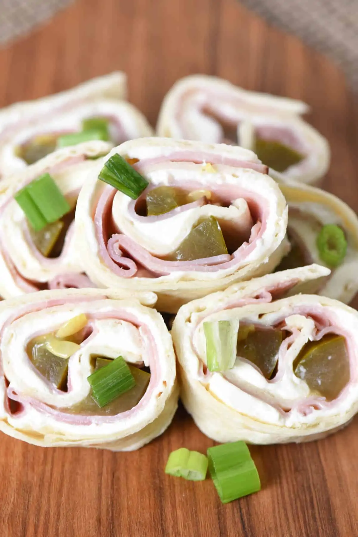 ham and dill pickle pinwheels piled on wooden cutting board