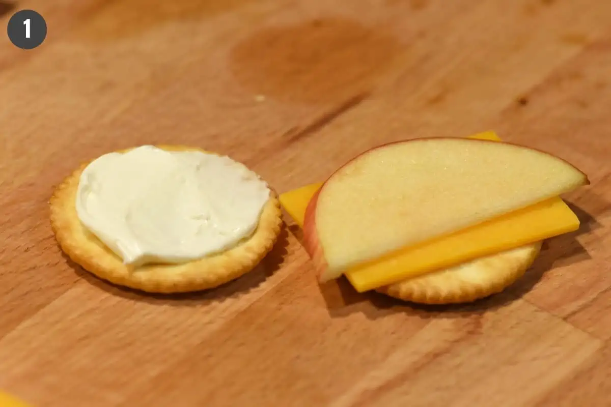 stacking apple slice and cheddar with cream cheese on Ritz crackers