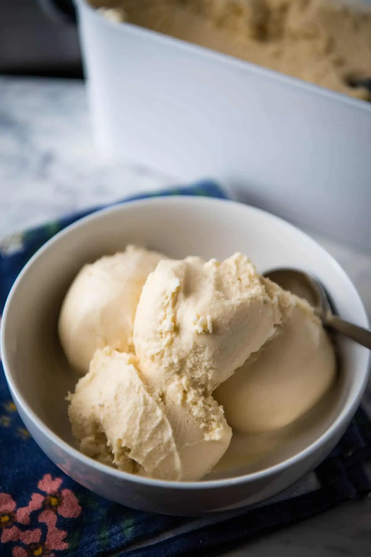 scoops of homemade vanilla ice cream without eggs in white bowl on blue cloth