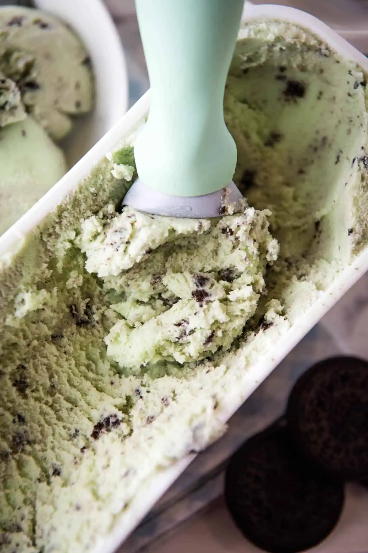 scooping mint cookies and cream ice cream out of white ice cream container