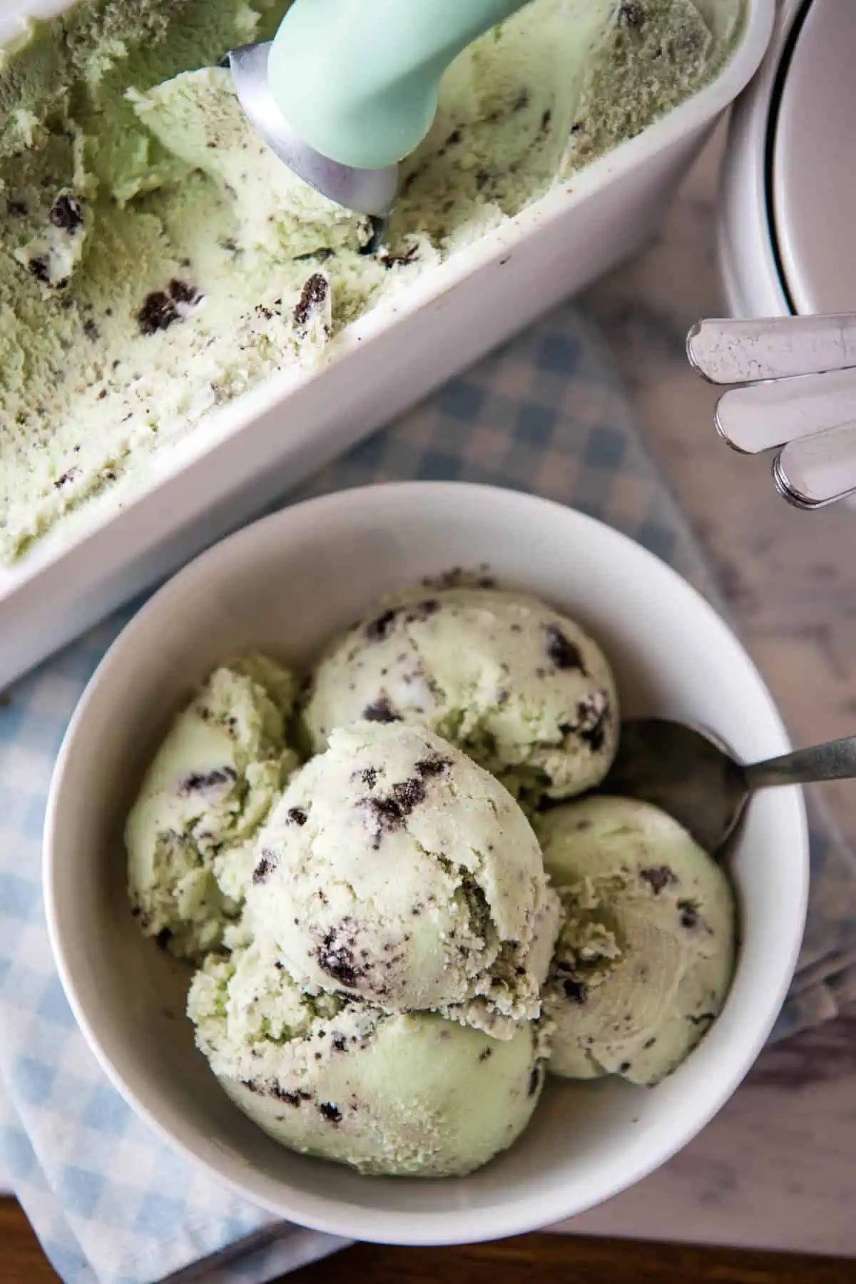 scoops of mint Oreo ice cream in white bowl with spoon next to carton of ice cream