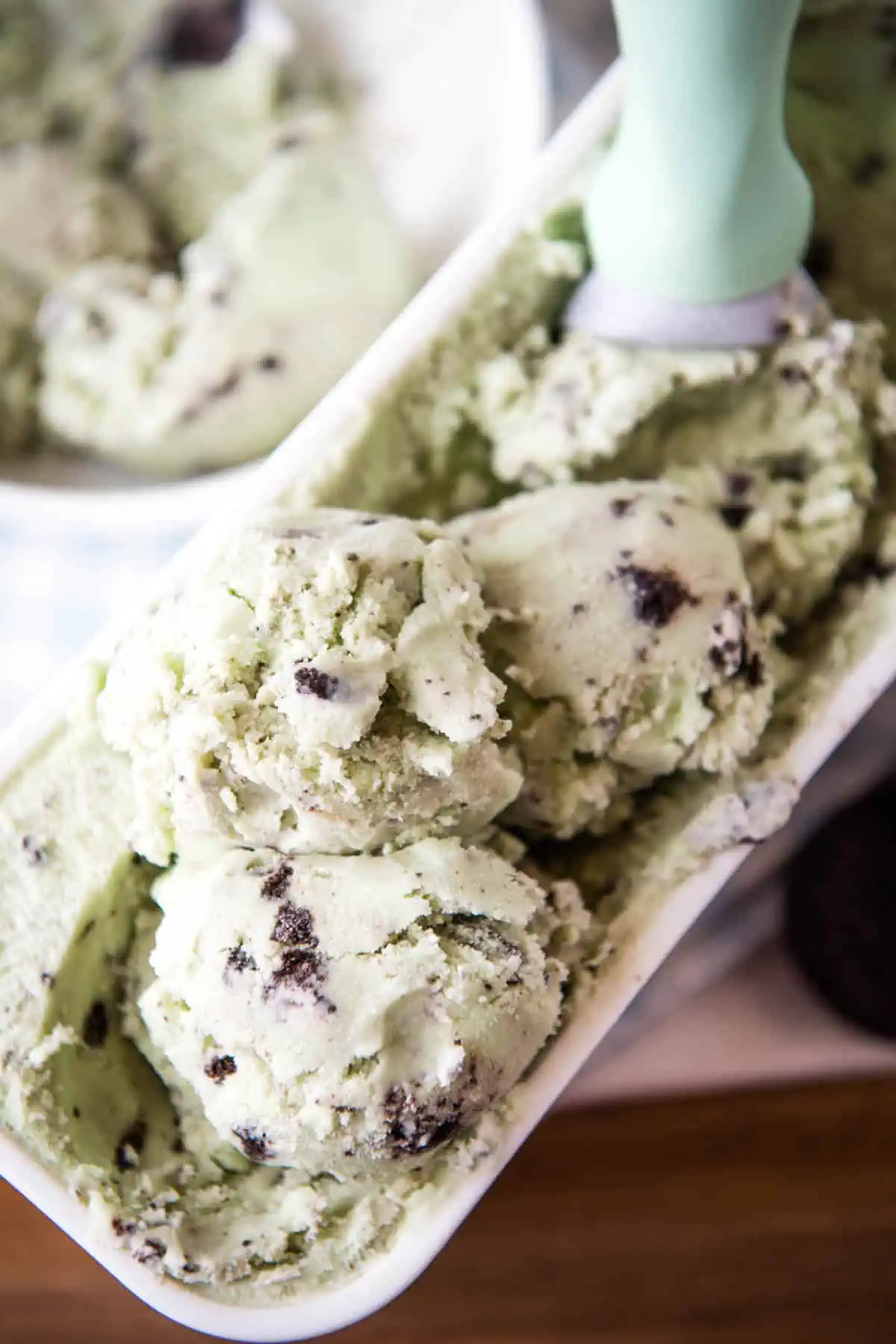 scoops of Oreo mint ice cream in white ice cream container with mint green ice cream scoop