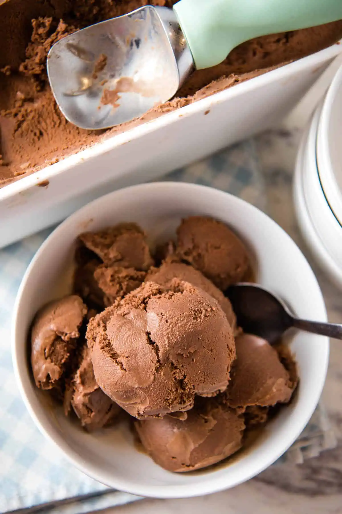 white bowl full of raw milk chocolate ice cream with spoon and ice cream scoop in ice cream container