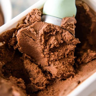 scooping homemade chocolate ice cream out of a large white rectangular ice cream freezer container