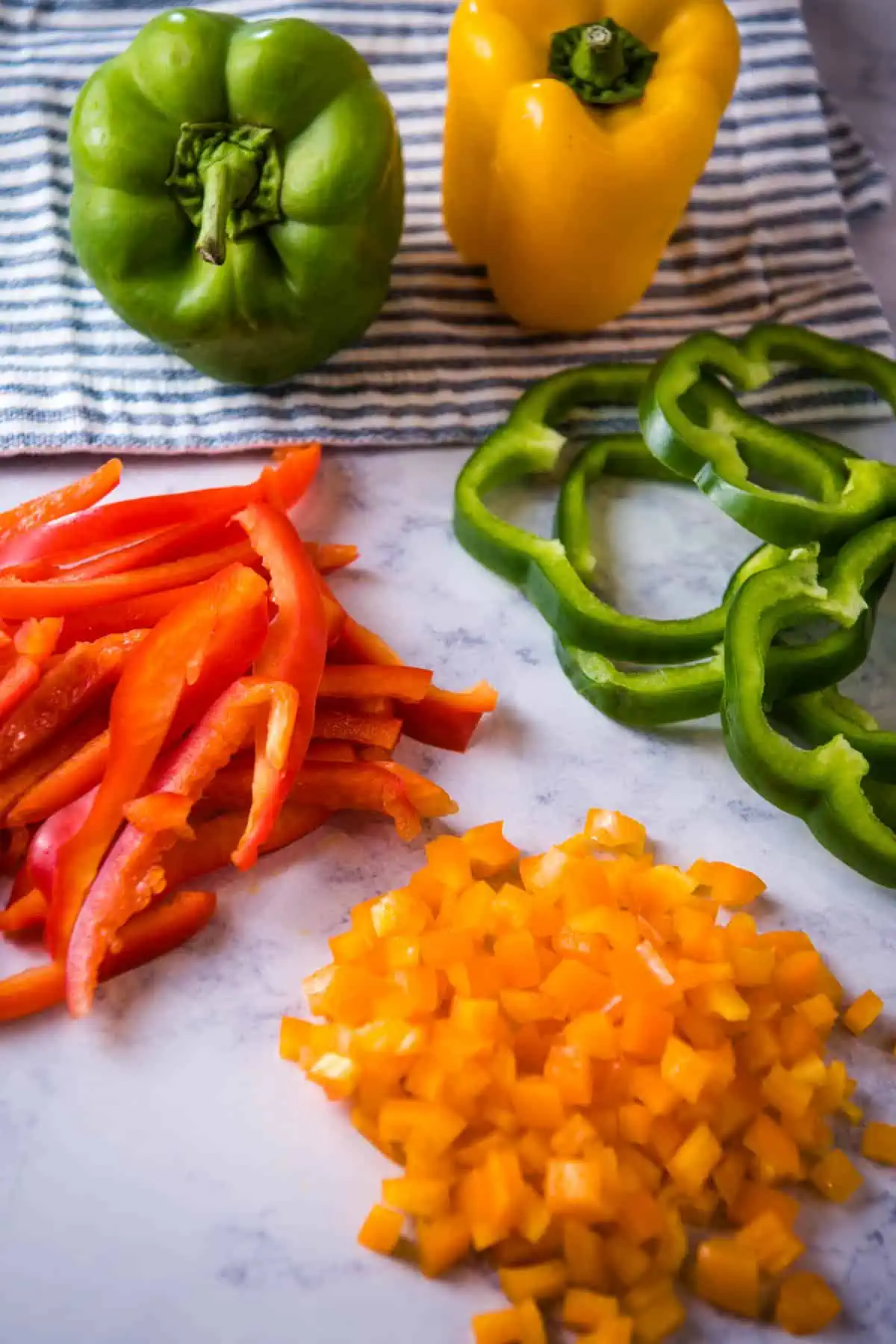 how to cut bell peppers by slicing or julienne, dicing, or rings on white marble countertop with blue striped towel