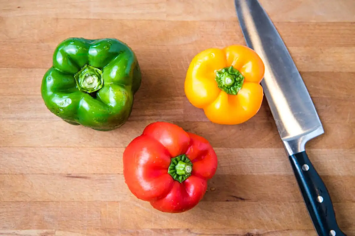 how to cut a bell pepper, including green, red, and yellow bell peppers on butcher block cutting board with chef's knife