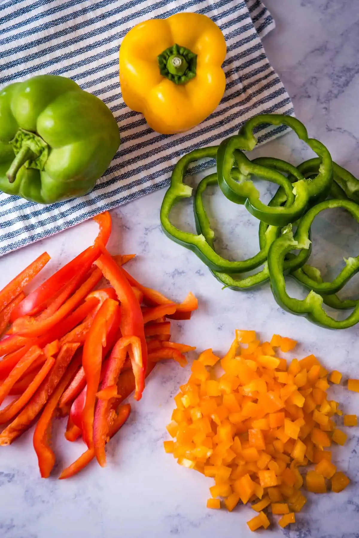 how to cut a pepper 4 ways, including julienne strips, diced, and rings with red, green, and yellow bell peppers on white marble countertop