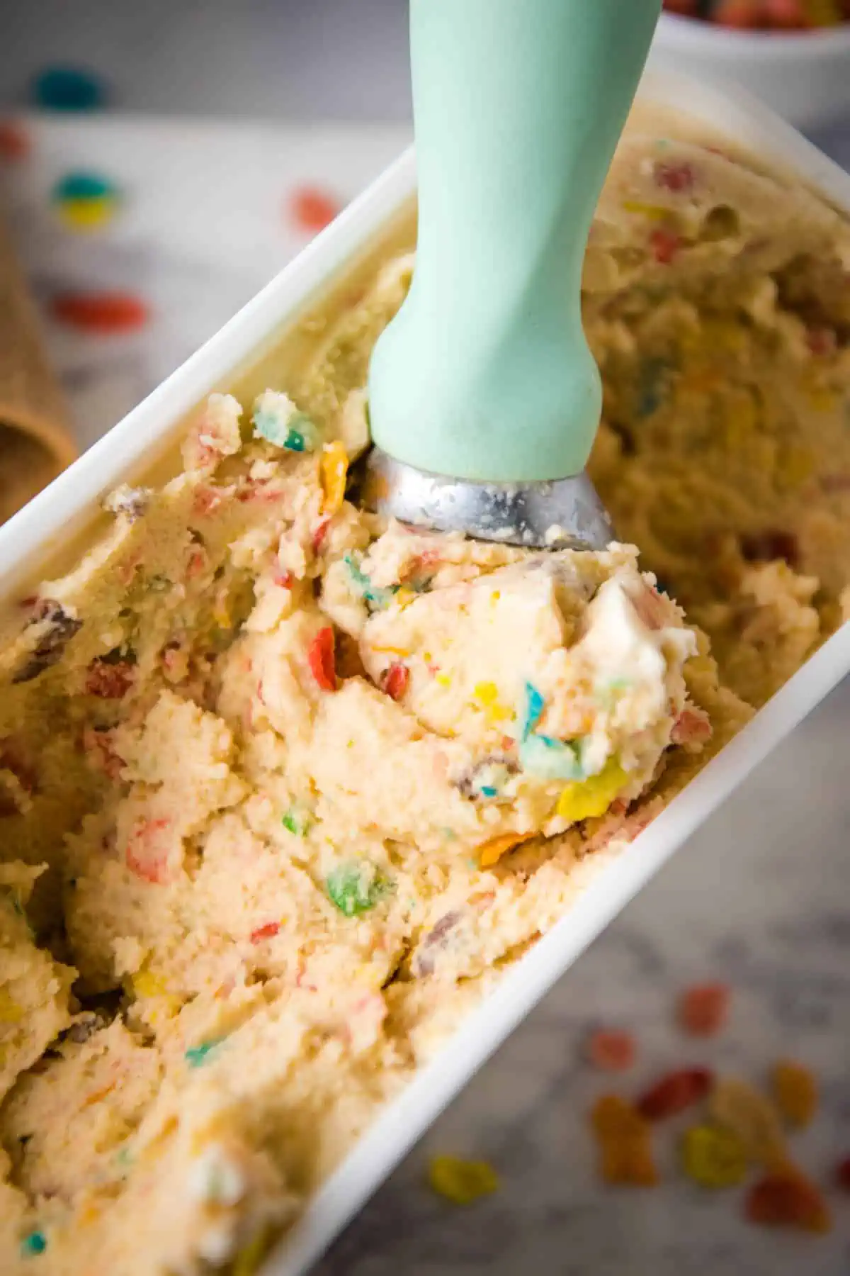 mint green ice cream scoop in white container of scoopable Fruity Pebbles cereal milk ice cream on white marble cutting board