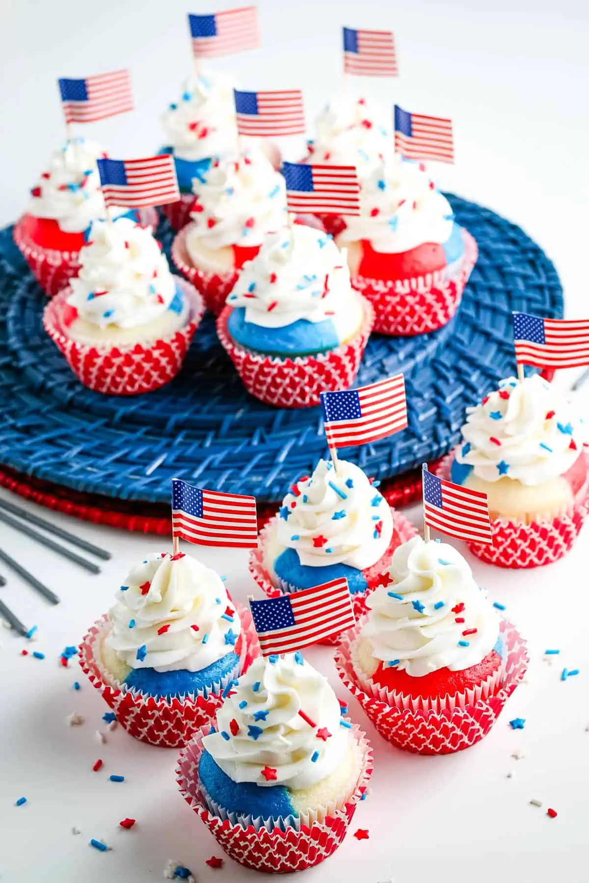 decorated red white and blue patriotic cupcakes with buttercream frosting, patriotic sprinkles, and flag toppers